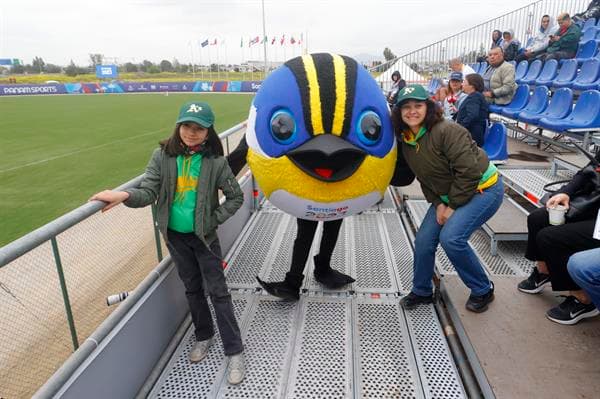 Aficionados fueron registrados este miércoles, 18 de octubre, al posar junto a la mascota de los Juegos Panamericanos 2023, Fiu, durante un partido de béisbol, en Santiago de Chile. EFE/Esteban Garay