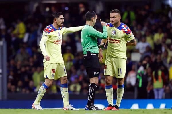 - Diego Valdés (i) y Jonathan Rodríguez (d) del América reclaman al árbitro central César Arturo Ramos (c), durante un juego de vuelta por las semifinales del torneo Apertura 2023 de la Liga MX, este 9 de diciembre de 2023. EFE/Sáshenka Gutiérrez