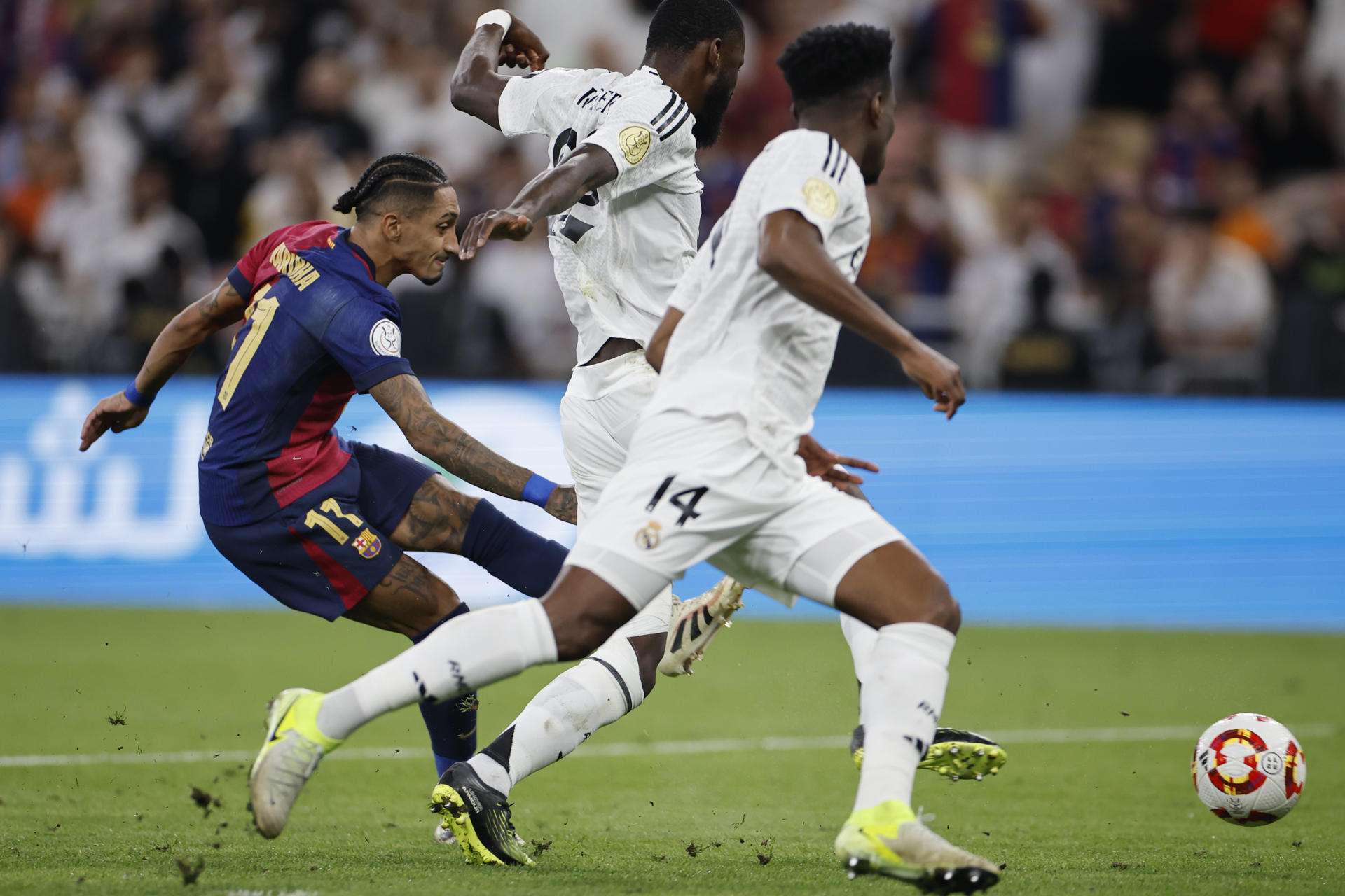 El delantero brasileño del Barcelona Raphinha consigue el quinto gol de su equipo frente a los madridistas Antonio Rudiger (C) y Aurelien Tchouameni (D), durante la final de la Supercopa de España disputada el 12 de enero del pasado año en Yeda, Arabia Saudí. EFE/ Alberto Estévez