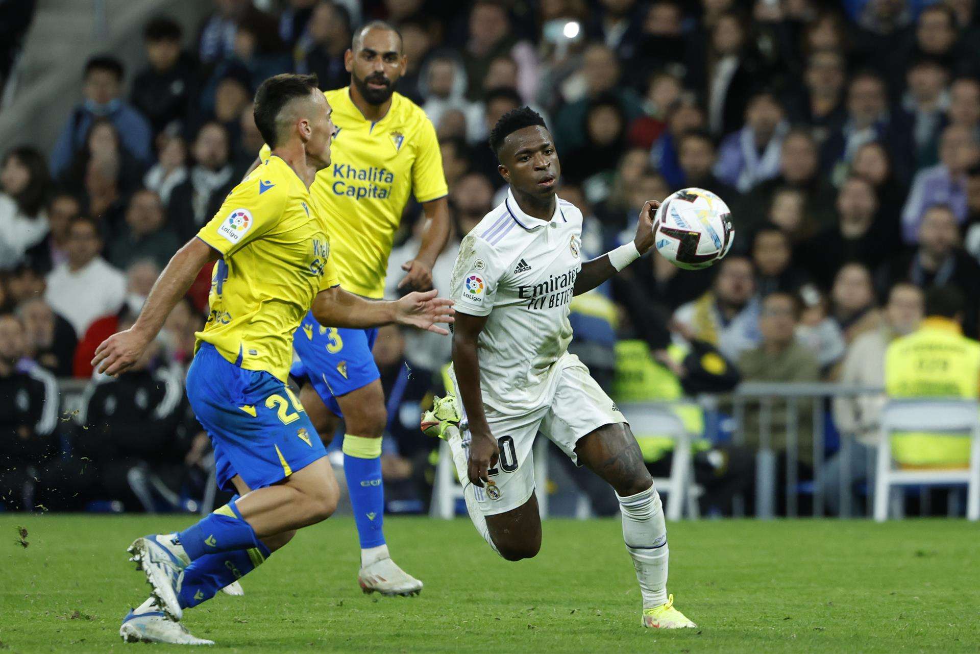 El delantero brasileño del Real Madrid, Vinicius Jr., disputa el balón ante el centrocampista del Cádiz, Fede San Emeterio, durante el encuentro correspondiente a la jornada 14 de primera división que disputan en el estadio Santiago Bernabéu, en Madrid. EFE / Juanjo Martín.